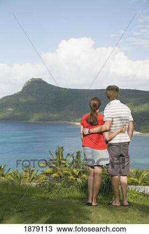 Stock Image - Couple At Edge Of Cliff Looking At Coastline. Fotosearch