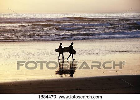 Stock Image - Couple Carrying Surfboards On The Beach In Silhouette. Fotosearch