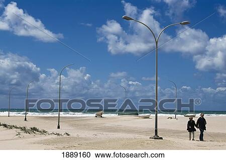 Stock Image - Couple Holding Hands Walking On Beach. Fotosearch