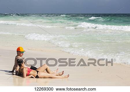 Couple laying and sitting on sandy beach with waves coming in and blue sky; Tulum, Quintana Roo, Mexico View Large Photo Image Stock Image - Couple laying and sitting on sandy beach with waves coming in and blue sky; Tulum, Quintana Roo, Mexico. Fotosearch