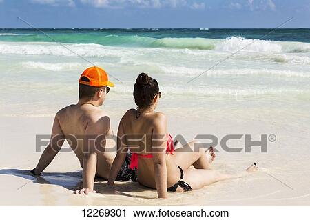 Couple laying and sitting on sandy beach with waves coming in and blue sky; Tulum, Quintana Roo, Mexico View Large Photo Image Stock Image - Couple laying and sitting on sandy beach with waves coming in and blue sky; Tulum, Quintana Roo, Mexico. Fotosearch