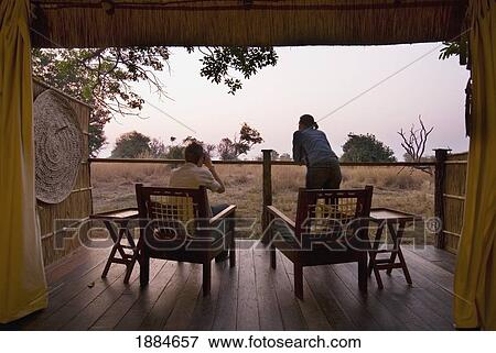 Stock Photo - Couple Looking Out From Room Of Safari Lodge At Dawn. Fotosearch