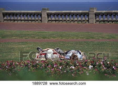 Stock Photo - Couple Lying Down In Park By Sea. Fotosearch