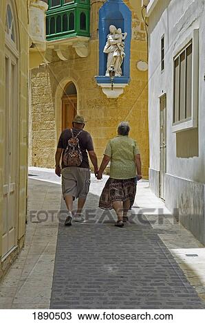 Stock Image - Couple Of Tourist Holding Hands Walking On Narrow Street. Fotosearch