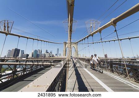 Stock Photography - Couple on a tandem bicycle on the pedestrian walkway on the Brooklyn Bridge, New York City, New York, United States. Fotosearch