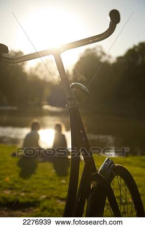 Stock Photo - Couple relaxing beside lake in the Vondelpark in the evening; Amsterdam, Holland. Fotosearch