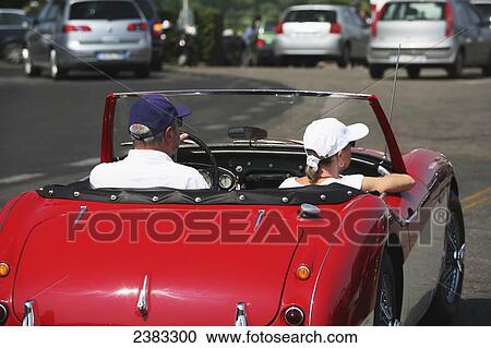 Stock Image - Couple sitting in car at vintage car and motorbike rally on large square Piazzale Michelangelo overlooking Florence city; Tuscany, Italy. Fotosearch