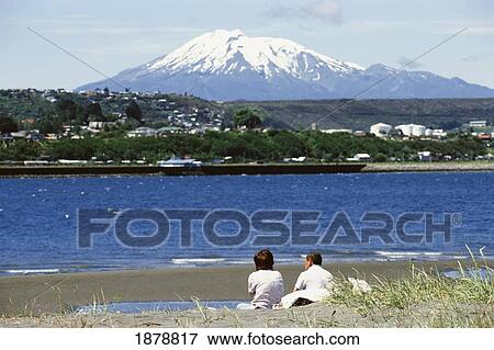 Stock Photo - Couple Sitting On Shore By Snow-Covered Mountain And Lake. Fotosearch