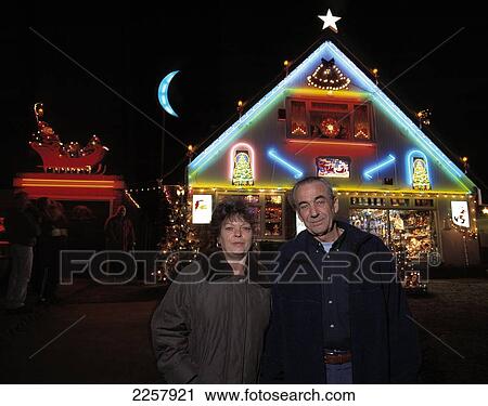 Stock Image - Couple Standing Outside House Decorated For Christmas (Christmas Lights And Decorations), Uk.. Fotosearch