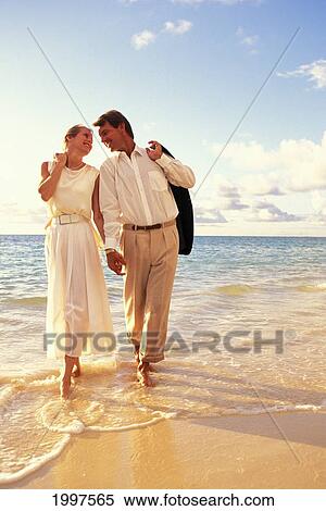 Stock Photography - Couple Walk In Shoreline Waters, Hold Hands And Look At Each Other, Warm Lighting. Fotosearch
