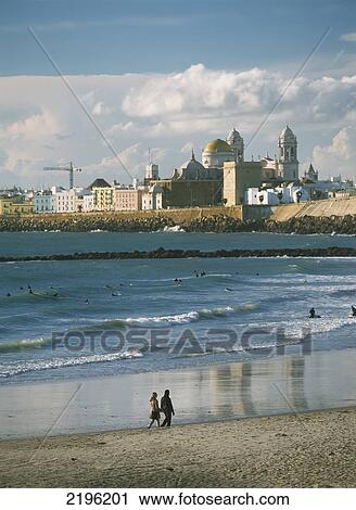 Couple Walking Along Beach In Front Of Surfers On Beach And Santa Cruz Cathedral, Cadiz, Andalucia, Spain. View Large Photo Image Stock Image - Couple Walking Along Beach In Front Of Surfers On Beach And Santa Cruz Cathedral, Cadiz, Andalucia, Spain.. Fotosearch