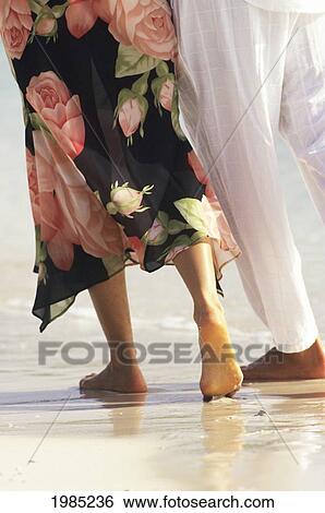 Stock Photograph - Couple Walking Along Sandy Beach, Detail Of Legs And Feet, View From Behind.. Fotosearch