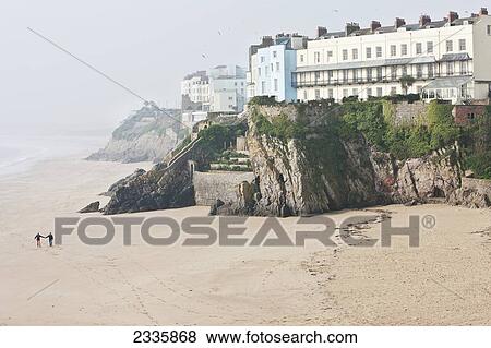 Stock Photo - Couple Walking Along South Beach; Tenby, Pembrokeshire Coast Path, Wales, United Kingdom. Fotosearch