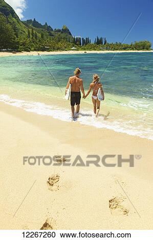 Stock Image - Couple walking into water with bodyboards; Kauai, Hawaii, United States of America. Fotosearch
