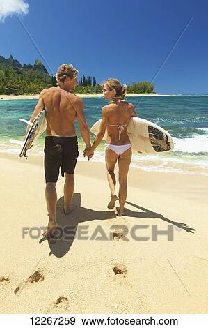 Stock Photo - Couple walking on beach with bodyboards; Kauai, Hawaii, United States of America. Fotosearch
