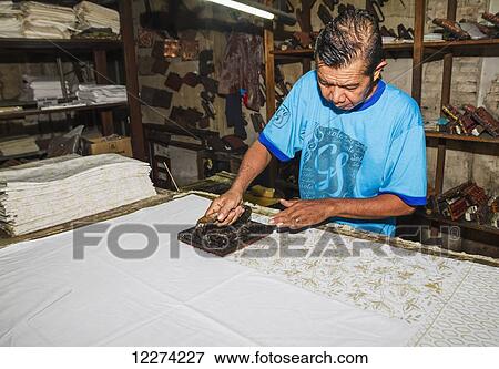 Stock Photo - Craftsman using a copper block stamp, called cap, to apply hot wax to a fabric in the production of printed batik at Gunawan Setiawan Batik Shop, Kampung Kauman, Surakarta (Solo), Central Java, Indonesia. Fotosearch