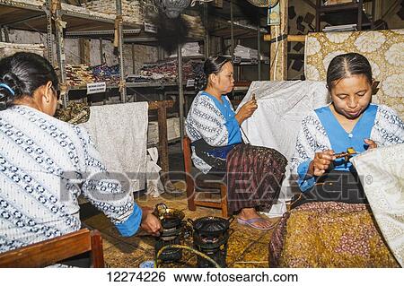 Stock Photograph - Craftswomen drawing intricate patterns by using a pen-like instrument, called canting, to apply hot wax to a fabric in the production of batik at Gunawan Setiawan Batik Shop, Kampung Kauman, Surakarta (Solo), Central Java, Indonesia. Fotosearch