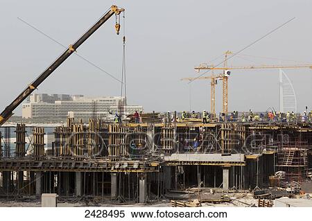 Stock Photography - Cranes at a building site with numerous workers working on the building; Dubai, United Arab Emirates. Fotosearch