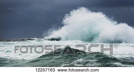 Stock Image - Crashing wave under dark storm clouds; Skeena-Queen Charlotte, British Columbia, Canada. Fotosearch