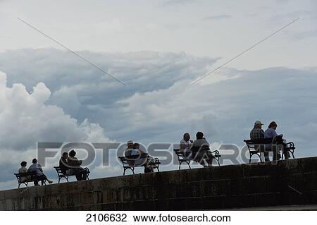 Stock Image - Croatia, Silhouettes of couples sitting on benches on sea wall; Dubrovnik. Fotosearch