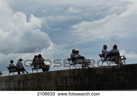 Stock Image - Croatia, Silhouettes of couples sitting on benches on sea wall; Dubrovnik. Fotosearch