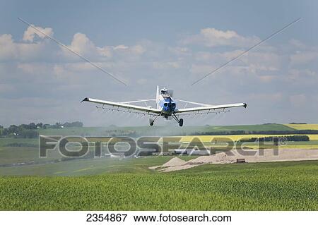 Stock Photo - Crop Dusting Plane Over Field With Blue Sky And Clouds; Crossfield, Alberta, Canada. Fotosearch