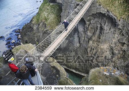 Stock Photo - Crossing Carrick-a-Rede rope bridge, a suspension bridge which spans 20 metres from the mainland to the tiny Carrick Island; County Antrim, Ireland. Fotosearch