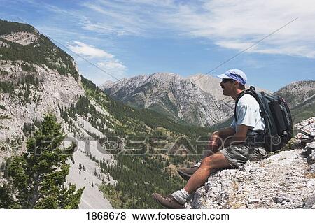 Stock Photo - Crowsnest Pass, Alberta, Canada; A Male Hiker Sits On A Ridge Looking At Turtle Mountain. Fotosearch