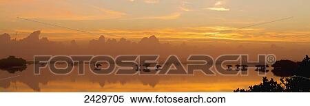 Stock Photography - Cumulus clouds above horizon at sunrise reflected in mangrove estuary, Merritt Island National Wildlife Refuge, near Titusville; Florida, United States of America. Fotosearch