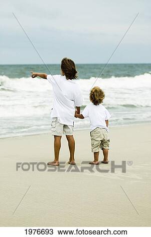 Stock Image - Cute Young Boys On The Beach, Looking At The Ocean Holding Hands.. Fotosearch