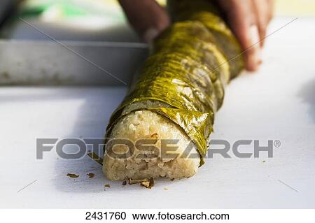 Stock Image - Cutting Lemang, traditional Indonesian food made of glutinous rice, coconut milk and salt that is cooked in a hollowed bamboo stick lined with banana leaves, Simalungun, North Sumatra, Indonesia. Fotosearch