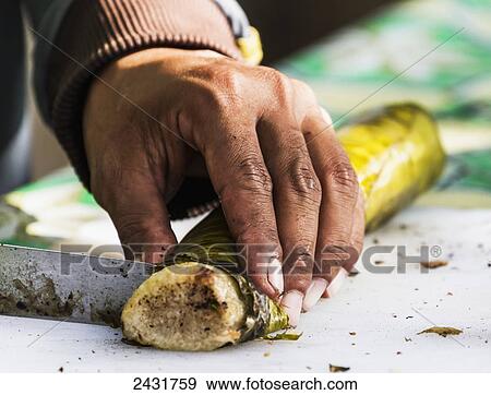 Stock Photo - Cutting Lemang, traditional Indonesian food made of glutinous rice, coconut milk and salt that is cooked in a hollowed bamboo stick lined with banana leaves, Simalungun, North Sumatra, Indonesia. Fotosearch