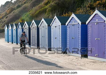 Stock Image - Cyclist On Bike Cycling By Beach Huts At Bournemouth Beach; Bournemouth, Dorset, England. Fotosearch