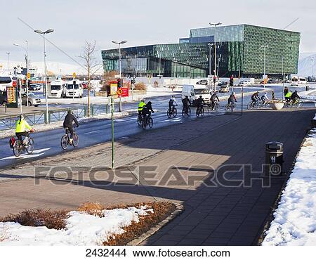 Picture - Cyclists biking in Reykjavik with Harpa Concert Hall and Conference Centre in the background; Reykjavik, Iceland. Fotosearch