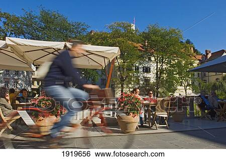 Stock Photograph - Cyclists Passing The Riverside Cafes, Ljubljana Slovenia. Fotosearch