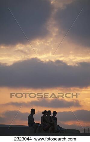 Cyprus, Paphos, Four people sitting on ledge at sunset View Large Photo Image Picture - Cyprus, Paphos, Four people sitting on ledge at sunset. Fotosearch