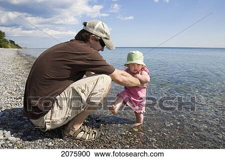 Dad Holding His Baby Daughter As She Hesitates To Wade In The Water Of Lake Ontario; Ontario Canada View Large Photo Image Stock Image - Dad Holding His Baby Daughter As She Hesitates To Wade In The Water Of Lake Ontario; Ontario Canada. Fotosearch