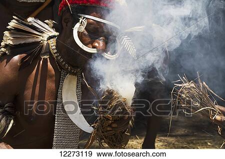 Dani men wearing an elaborate headdress of bird of paradise or cassowary feathers lighting a fire, Obia Village, Baliem Valley, Central Highlands of Western New Guinea, Papua, Indonesia View Large Photo Image Stock Photo - Dani men wearing an elaborate headdress of bird of paradise or cassowary feathers lighting a fire, Obia Village, Baliem Valley, Central Highlands of Western New Guinea, Papua, Indonesia. Fotosearch