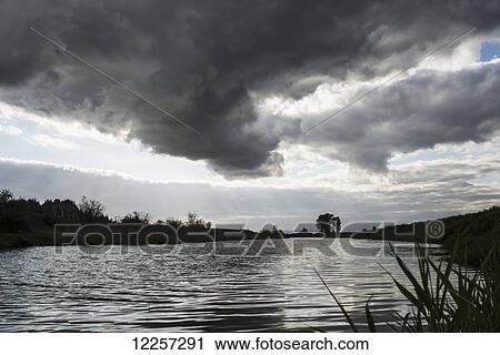 Stock Image - Dark storm clouds gather along the Alouette River; Pitt Meadows, British Columbia, Canada. Fotosearch