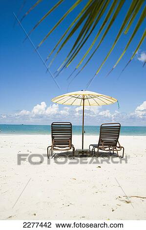 Stock Image - Deck Chairs Under Parasol On White Sandy Beach With Palm Trees Overlooking Blue Sea. Pantai Cenang (Cenang Beach), Pulau Langkawi, &#10; Malaysia, South East Asia.. Fotosearch