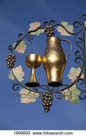 Stock Image - Decorative Gold Sign Of A Goblet, Vase And Grapes Against A Blue Sky; Breisach Am Rhein, Germany. Fotosearch