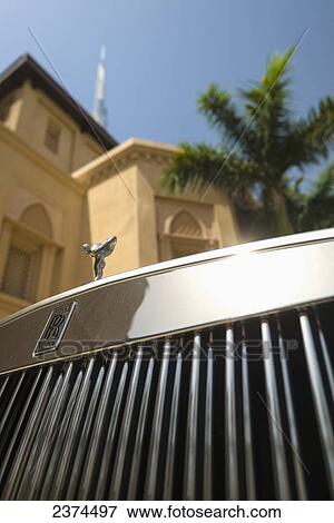 Stock Photo - Detail of chrome plated Rolls Royce beneath palm tree and traditional arabic style hotel with the Burj Khalifa behind; Dubai, United Arab Emirates. Fotosearch