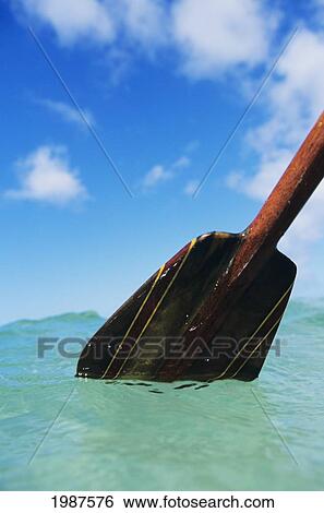 Stock Photograph - Detail Of Paddle Stroking Surface Of Water, Turquoise Ocean, Blue Sky And Clouds.. Fotosearch