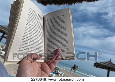 Detail of someone reading a paperback book on a sun lounger on the beach; Djerba, Tunisia View Large Photo Image Stock Photo - Detail of someone reading a paperback book on a sun lounger on the beach; Djerba, Tunisia. Fotosearch