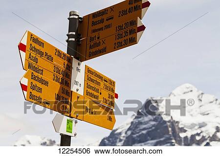 Stock Photograph - Distances and destinations on a sign with a snowcapped mountain in the background; Grindelwald, Bernese Oberland, Switzerland. Fotosearch