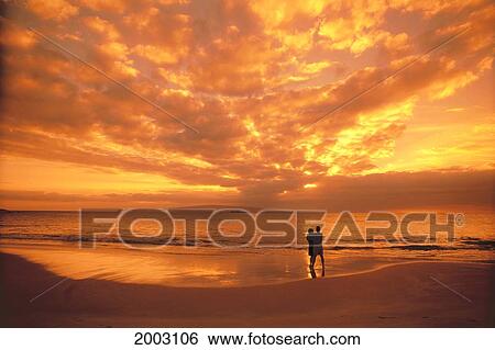 Distant View Of Couple On Beach At Sunset, Fiery Orange Sky And Clouds View Large Photo Image Stock Photograph - Distant View Of Couple On Beach At Sunset, Fiery Orange Sky And Clouds. Fotosearch
