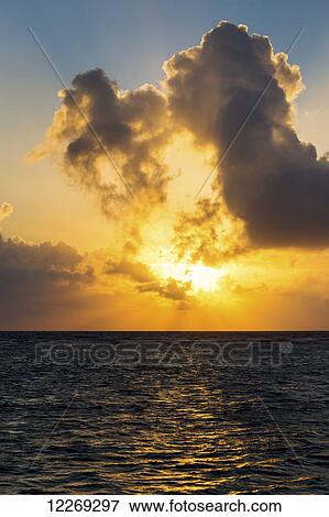 Stock Photo - Dramatic colourful sky at sunrise reflecting off ocean with backlit clouds and blue sky; Akumal, Quintana Roo, Mexico. Fotosearch