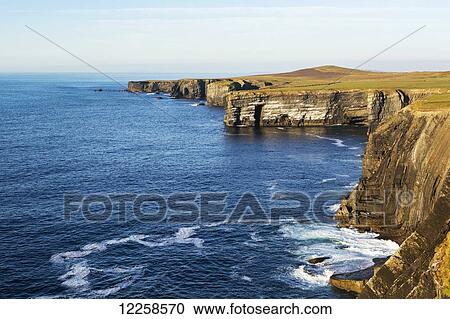 Dramatic rock cliffs along the shoreline at sunset with blue sky; Kilkee, County Clare, Ireland View Large Photo Image Stock Image - Dramatic rock cliffs along the shoreline at sunset with blue sky; Kilkee, County Clare, Ireland. Fotosearch