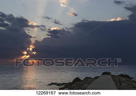 Dramatic sky with sun rays breaking through dark storm clouds at sunset over the horizon; Paphos, Cyprus View Large Photo Image Stock Photo - Dramatic sky with sun rays breaking through dark storm clouds at sunset over the horizon; Paphos, Cyprus. Fotosearch