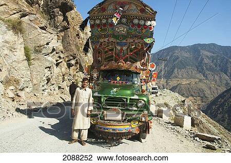 Stock Image - Driver Standing In Front Of His Painted And Decorated Pakistani Truck Near Dasu, North-West Frontier Province, Pakistan. Fotosearch